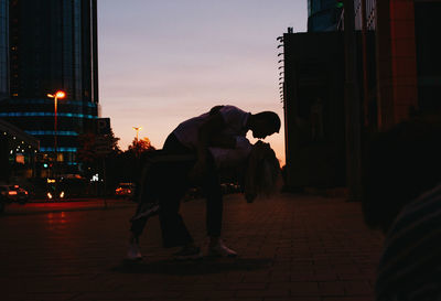 Man on footpath by street against sky during sunset