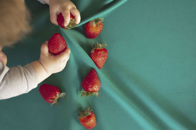 Cropped baby' hands holding strawberries on the turquoise background 