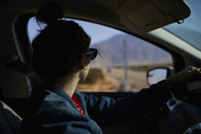 Close-up of young woman looking through window while sitting in car
