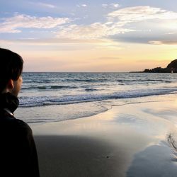 Rear view of man looking at sea against sky during sunset