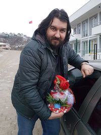 Portrait of man holding gift standing by car outdoors