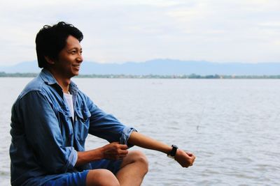 Smiling man sitting by sea against sky