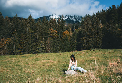 Young woman sitting in the middle of a green pasture in mountains.