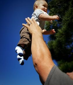Cropped image of father throwing son against blue sky