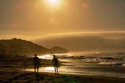 Silhouette people on beach against sky during sunrise