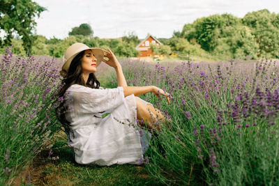 Close up of beautiful smiling woman in hat sitting on grass in lavender field 