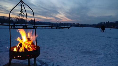 Bonfire on snowcapped landscape against sky during dusk