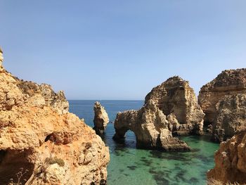 Panoramic shot of rocks in sea against clear blue sky