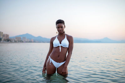 African american female in sea water looking at camera on background of sunset sky