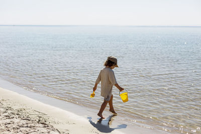 Boy at sea walking at sandy beach barefoot