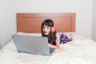 Young woman using digital tablet while sitting on bed at home