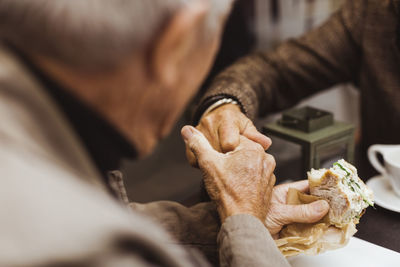 Senior man holding hand of woman while having sandwich at cafe during weekend