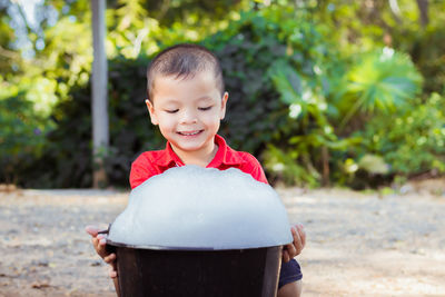 Smiling boy with soap sud in bucket sitting on land