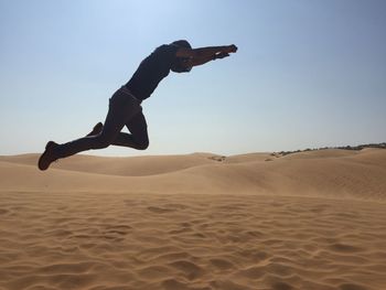 Full length of man jumping in desert against clear sky