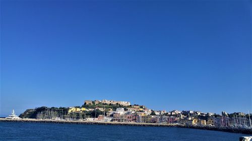 View of buildings by sea against clear blue sky