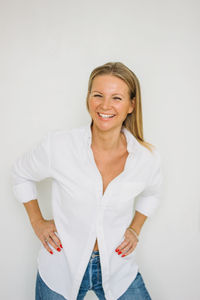 Portrait of happy blonde forty year woman with long hair in white shirt on the white wall background 