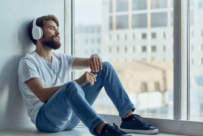 Young man listening music sitting by window