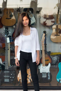 Portrait of young woman standing against guitar store