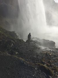 Mid distance of man standing on cliff against waterfall