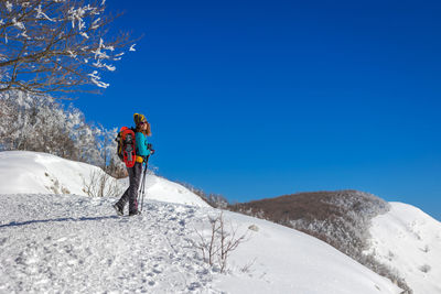 Snow hiker in the mountains, with snowshoes and ski poles, backpack and hat. 
