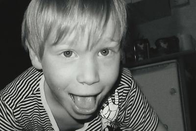 Close-up portrait of playful boy showing tongue at home
