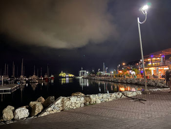 Illuminated city by river against sky at night