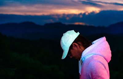 Man with fluorescent baseball cap against mountain at sunset