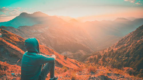 Rear view of man sitting on mountain during sunset