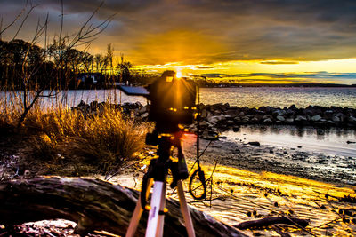 Close-up of camera by sea against sky during sunset