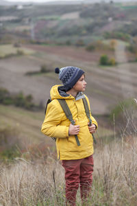 Little boy with a backpack standing on a hill in autumn day and looking away.