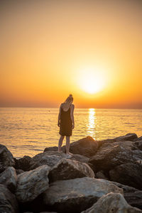 Rear view of man standing on rock against sea during sunset