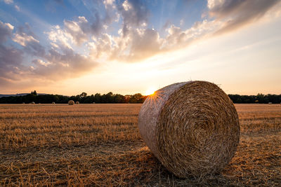 Hay bales on field against sky during sunset