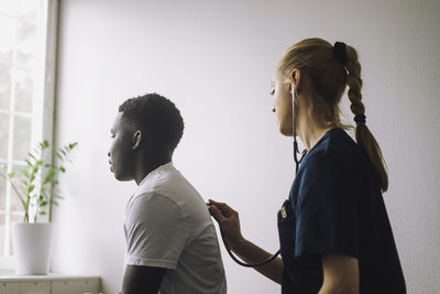 Side view of female nurse examining male teenage patient in clinic