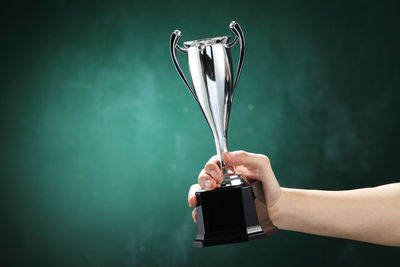 Cropped hand of woman holding trophy against green wall