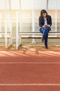 Full length of young woman sitting against fence