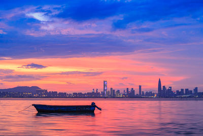 Boat on sea against city and dramatic sky during sunset