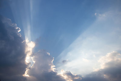 Low angle view of sunlight streaming through clouds