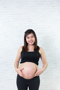 Portrait of smiling pregnant woman standing against wall