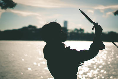 Woman practicing with knife against sea during sunset