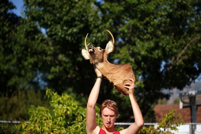 Young man holding hunting trophy against trees