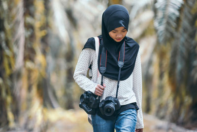 Teenage girl carrying camera against trees