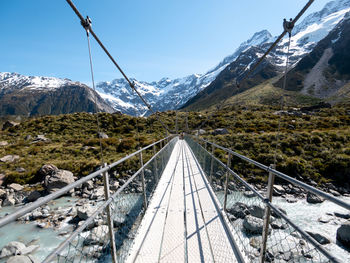 Footbridge over river against snowcapped mountains 