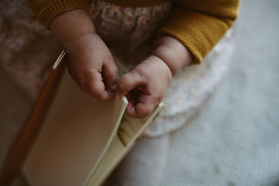 Midsection of baby holding book while sitting on bed