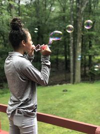 Full length of young woman in park having fun with bubbles 