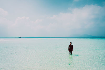 Rear view of man standing in sea against sky