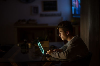 Side view of boy using laptop on table at night