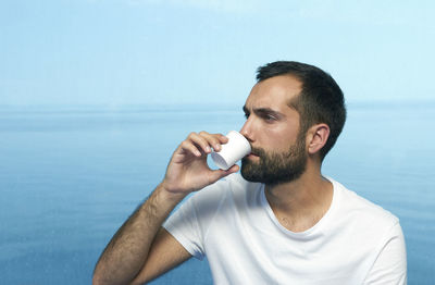 Young man drinking coffee in cruise ship against sea