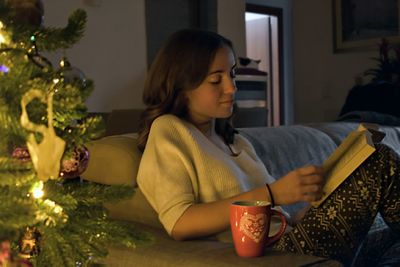 Young woman looking at while sitting on christmas tree at home