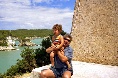 Full length of father and little son sitting on shore