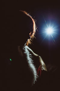 Woman sitting against illuminated light in dark